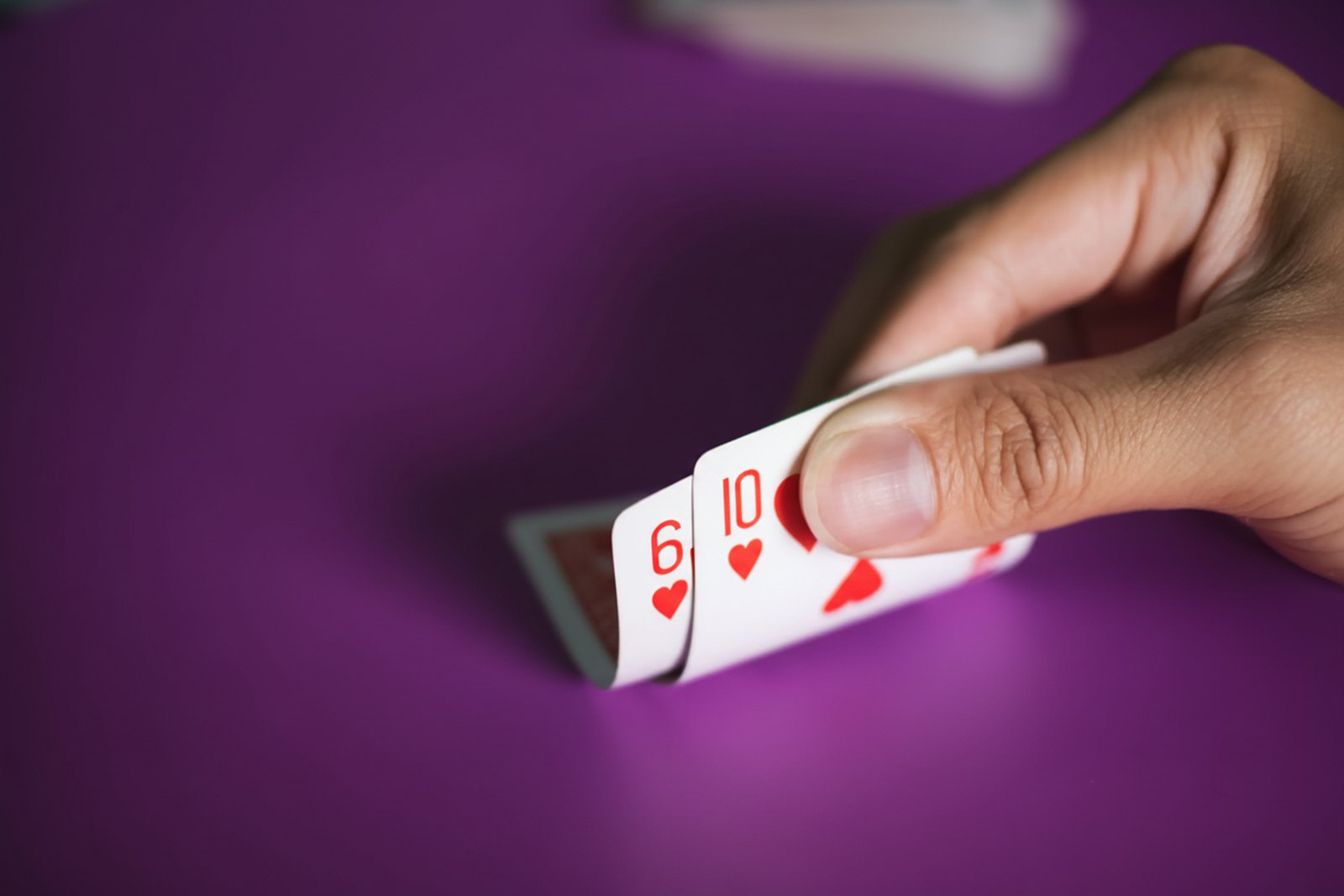 Mão de jogador levantando as cartas 6 e 10 de copas sobre a mesa de poker
